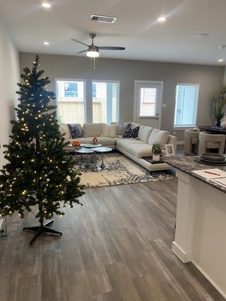 Modern living area with a plush sectional, holiday decor, wood floors, and bright windows creating a welcoming ambiance.
