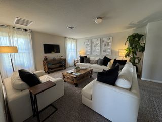 A cozy living room with plush white sofas, dark pillows, soft lighting, and modern wall art.