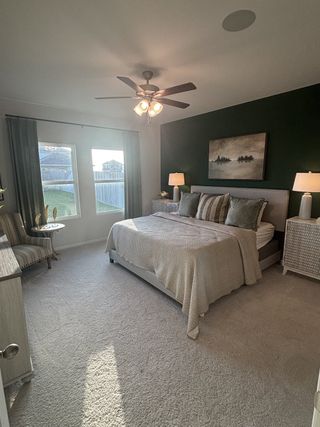 A cozy bedroom featuring a dark accent wall, elegant bedding, and warm lighting from a modern ceiling fan.