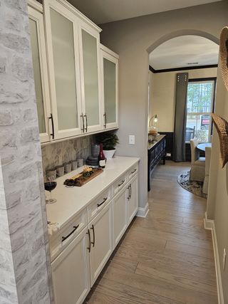 A sleek butler’s pantry with frosted glass cabinets, quartz counters, and elegant backsplash leading to the dining area.