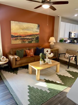 A cozy living room with a brown leather sofa, abstract art, and a geometric rug, featuring warm lighting and natural wood accents.