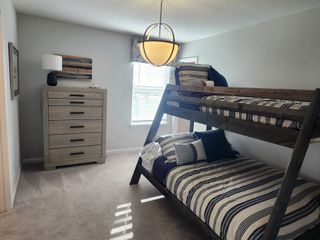 A cozy bedroom featuring a sleek bunk bed, striped bedding, a textured dresser, and warm, modern lighting.