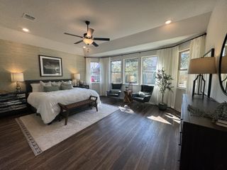 A spacious bedroom with a cozy bed, elegant wood flooring, large windows, and stylish seating, all under warm lighting.