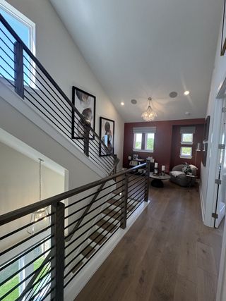 A modern hallway with wood flooring, chic railings, a cozy seating nook, and stylish wall art, illuminated by natural light.