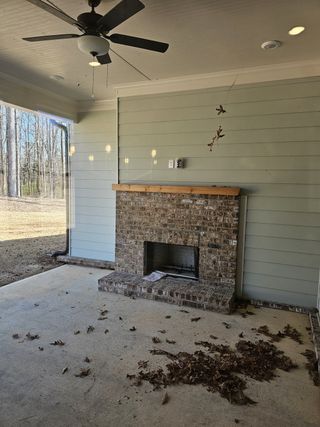 A cozy patio with a ceiling fan and brick fireplace, offering a serene view of the surrounding woods.