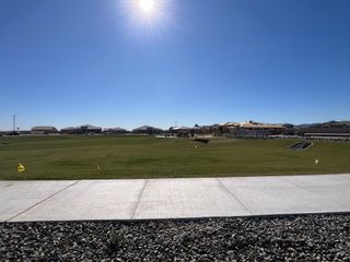 A sprawling green lawn and new homes under a clear blue sky at Sentiero at Windrose by David Weekley Homes (Waddell, AZ).