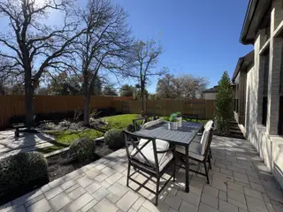 A serene patio with elegant outdoor seating, lush greenery, and a wooden fence backdrop for cozy, scenic gatherings.