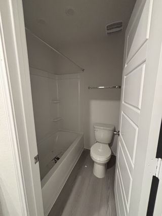 A compact bathroom featuring a white bathtub, sleek flooring, and classic white door for a clean, minimalist look.