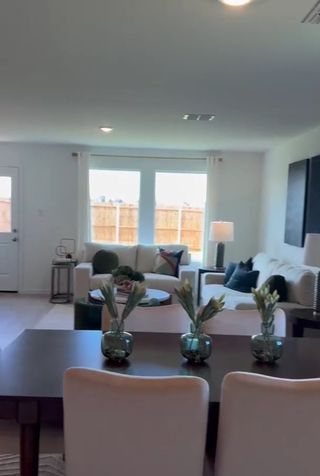 A bright living space with large windows, cozy seating, and a dining table adorned with vases and fresh flowers.