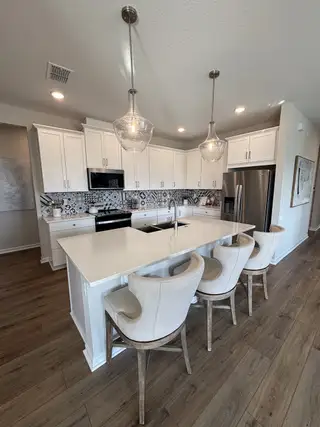 A modern kitchen with white cabinetry, patterned tile backsplash, and a spacious island with elegant pendant lighting.