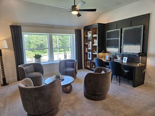 Model Home A cozy living room with plush chairs, a modern desk, and large windows offering a scenic view.
