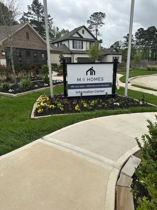 A charming brick home with vibrant landscaping in Moran Ranch by M/I Homes, featuring a welcoming information center (Willis, TX).