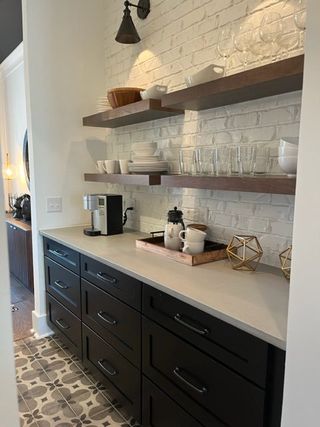 A chic kitchen nook with black cabinets, white brick backsplash, and open shelving displaying elegant dishware.