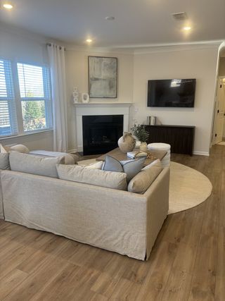 A cozy living room featuring a beige sofa, fireplace, wall art, and wood floors with abundant natural light.