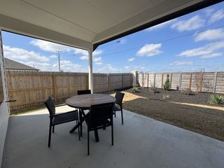 A cozy patio with a round wooden table and chairs, enclosed by a privacy fence and landscaped yard.