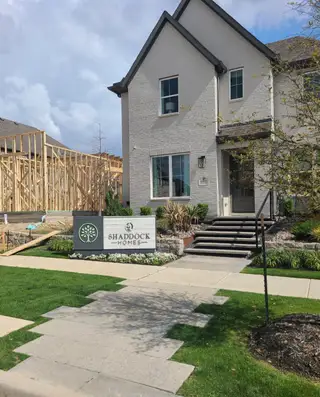 A charming white brick home with manicured landscaping at The Grove Frisco - 40' Lots by Shaddock Homes (Frisco, TX).