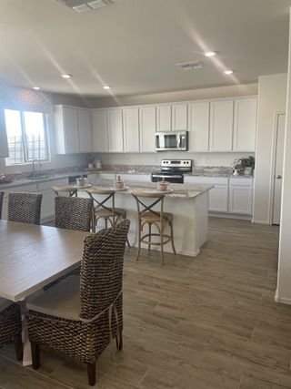 A spacious kitchen with white cabinets, granite countertops, and woven dining chairs. Modern and inviting ambiance.
