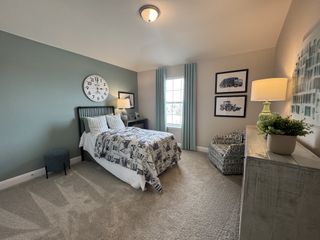 A charming bedroom with a round wall clock, a patterned comforter, a cozy armchair, and framed artwork, creating a playful and inviting space.