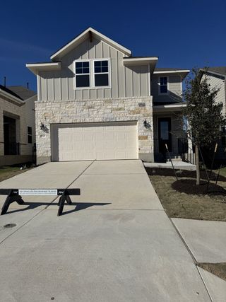 A modern beige home with stone accents and a spacious driveway in The Cottages at Lariat by Ashton Woods (Liberty Hill, TX).