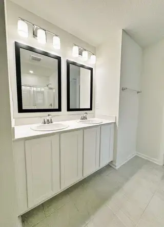 Model Home A bright bathroom with dual sinks, sleek black-framed mirrors, and modern lighting fixtures.