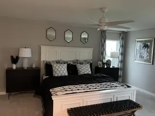 Stylish bedroom with a cozy bed, modern mirrors, a ceiling fan, and elegant black-and-white decor.
