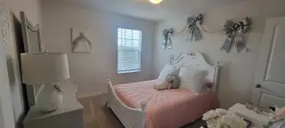 A charming bedroom with a white ornate bed frame, pink quilted bedding, and whimsical bow decor creates a sweet and inviting space.