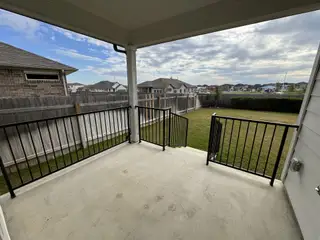 Model Home A covered patio with a black railing overlooks a spacious backyard, perfect for outdoor relaxation.