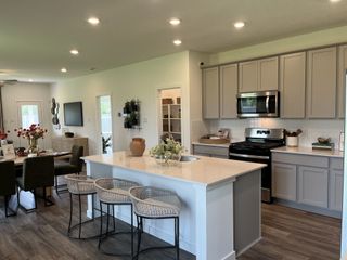 A modern kitchen features a spacious island, sleek gray cabinets, and stainless steel appliances, creating an inviting open layout.
