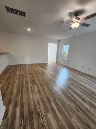 Model Home An open living room with sleek wood flooring, neutral walls, and a ceiling fan, offering abundant light and space.