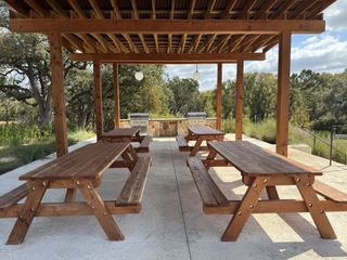 A serene outdoor picnic area with wooden tables and BBQ grills, surrounded by trees and nature.