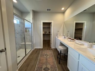Elegant bathroom with dual sinks, a spacious glass shower, and a walk-in closet, featuring warm wood floors.