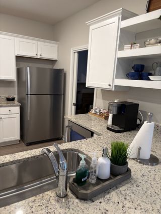 A modern kitchen with granite countertops, stainless steel appliances, and sleek white cabinets.