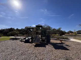 A sunny playground with slides and trees in Highland Village by Monticello Homes, Georgetown, TX.
