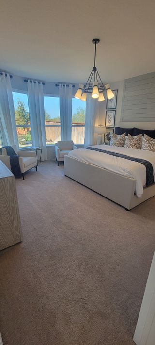 A spacious master bedroom featuring a modern chandelier, cozy sitting area, and large windows letting in natural light.