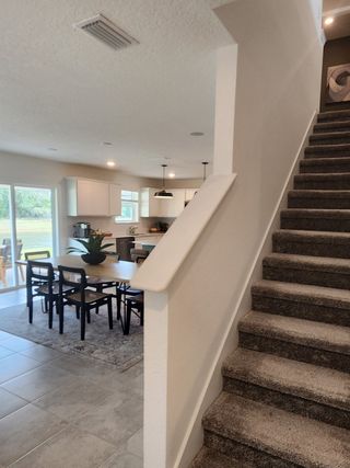 A modern kitchen viewed from carpeted stairs, featuring pendant lighting and a sleek dining setup.