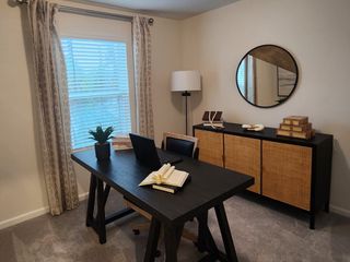 A cozy office with a dark wooden desk, modern lamp, round mirror, and woven cabinet, complemented by elegant curtains.
