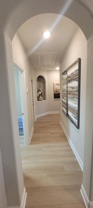 Model Home A welcoming hallway with elegant wood flooring, arched entry, modern artwork, and soft lighting.