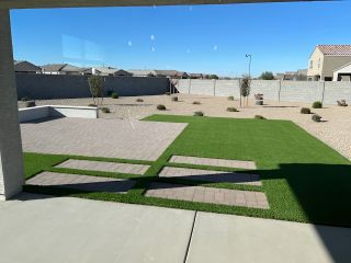 Model Home A modern backyard featuring a mix of paved and grassy areas with desert landscaping and clear blue skies.