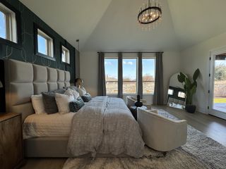 A cozy bedroom with a tufted headboard, modern chandelier, and large windows, featuring elegant decor and soft lighting.