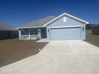 A light blue single-story suburban home with a two-car garage, white porch railing, and a spacious concrete driveway.
