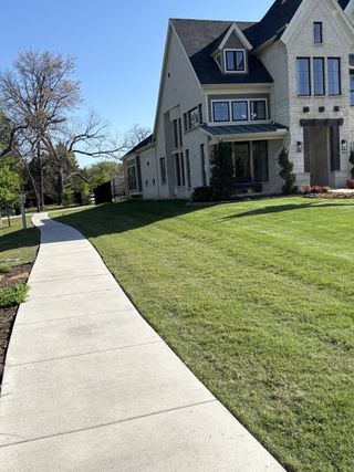 Street view A beautiful light brick home with large windows and lush lawn in Lake Shore Village by Grand Homes (Rowlett, TX).