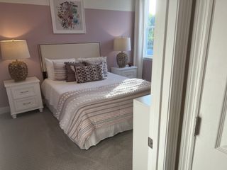 Model Home A cozy bedroom with soft pink accents, plush bedding, wicker lamps, and natural light filtering through a window.