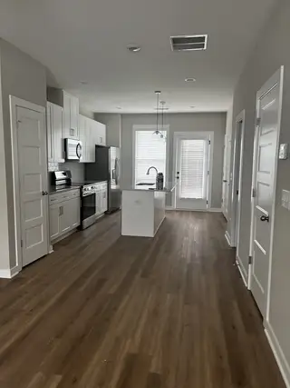 Model Home A modern kitchen with sleek white cabinets, stainless steel appliances, and rich wooden floors.