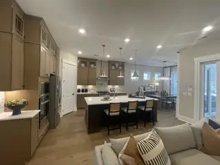 A modern kitchen with wood cabinets, a central island, and pendant lighting, seamlessly flowing into a cozy dining area.