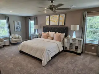 Model Home A spacious bedroom with elegant decor, featuring a plush bed, mirrored nightstands, and natural light from large windows.