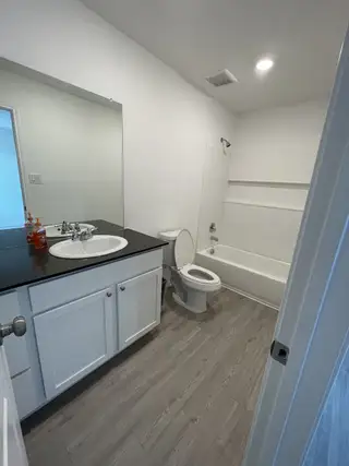 Model Home A modern bathroom featuring a sleek black countertop, white cabinetry, and wood flooring for a contemporary touch.
