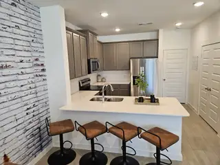 Model Home A modern kitchen with a white brick accent wall, sleek cabinets, and a cozy breakfast bar with stylish brown stools.