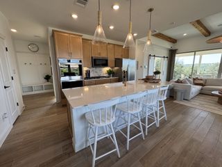 Model Home A stylish kitchen with a large island, white counter stools, and pendant lighting, flowing into a bright living area with rustic wood accents.