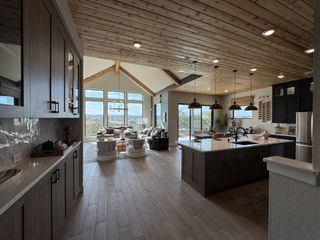 Model Home A spacious, open-concept living area with wood ceilings, modern kitchen, and large windows offering scenic views.
