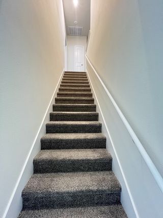 A carpeted staircase with neutral walls leads to a bright upper floor, showcasing modern, minimalist elegance.